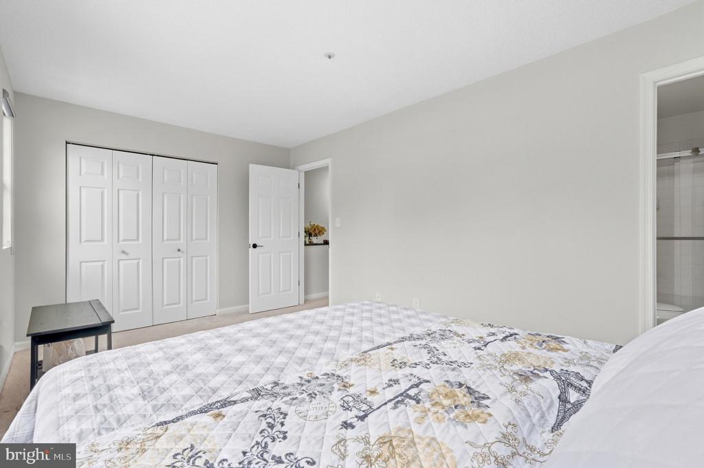 Bedroom with a patterned bed, white closet doors, and a bathroom doorway.