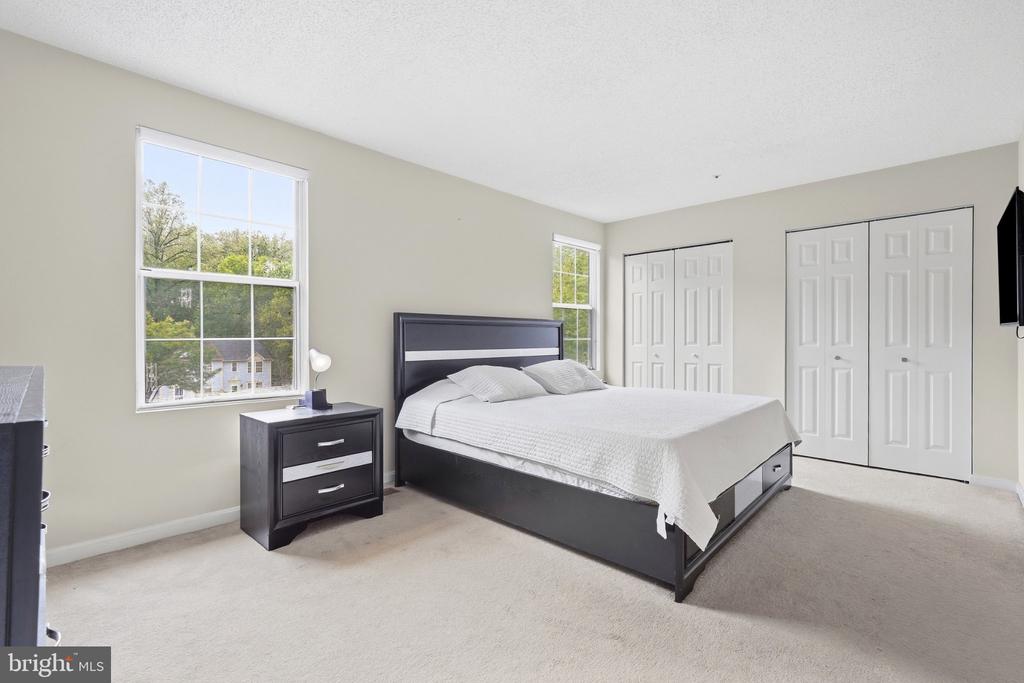 Bedroom with a large dark bed, white bedding, two windows, and white closet doors.