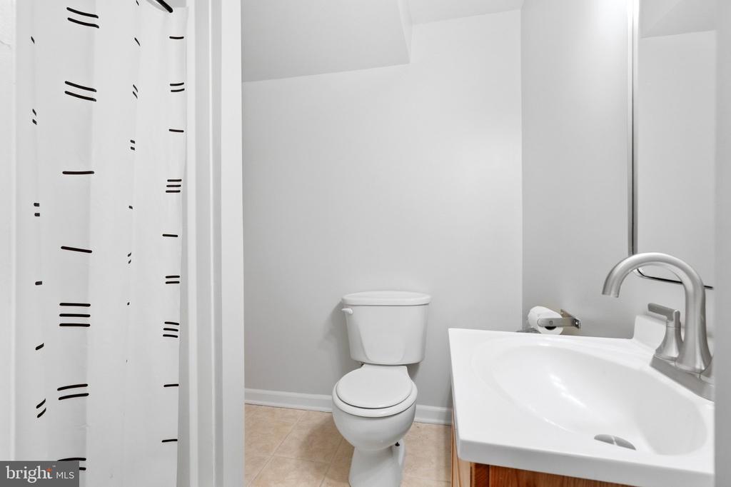 Bathroom with a white toilet, sink vanity, patterned shower curtain, and beige tile floor.