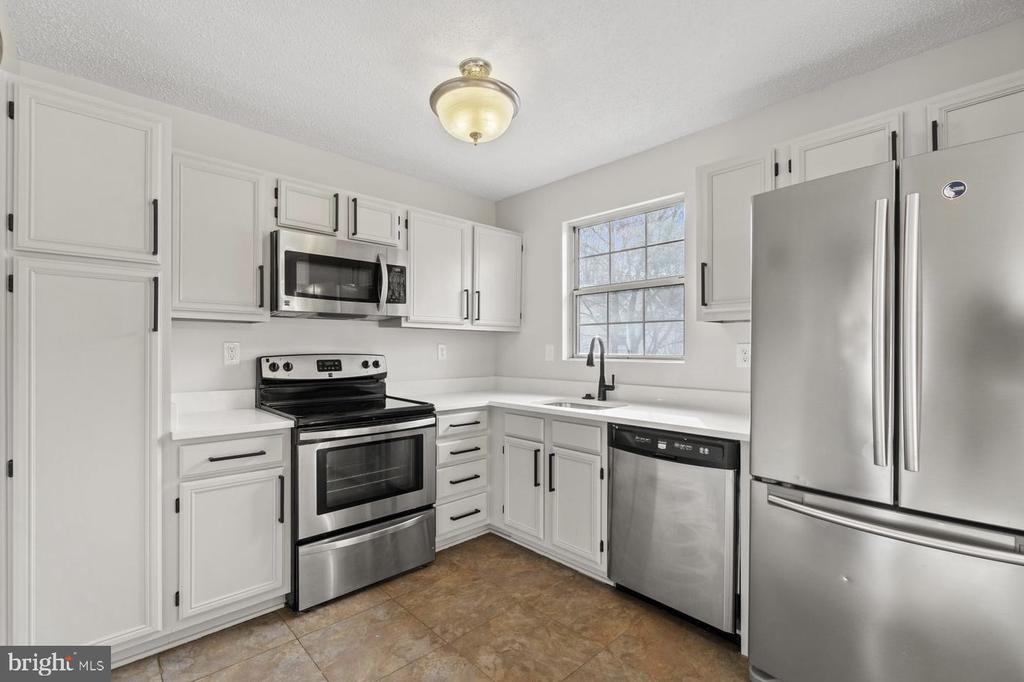 White kitchen with stainless steel appliances, a window above the sink, and tan tile flooring.