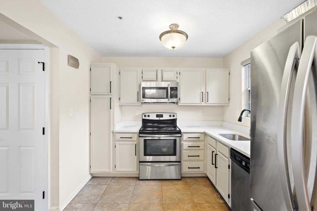 Kitchen with white cabinets, stainless-steel appliances, corner sink, and tan tile floor.