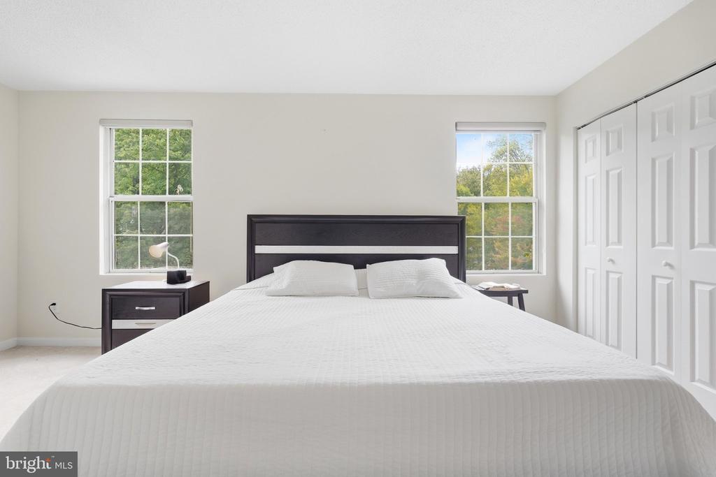 Bedroom with a large white bed, dark wood headboard, two windows, and white closet doors.