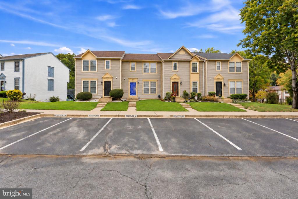 Row of tan townhouses with front lawns and reserved parking spaces in front.