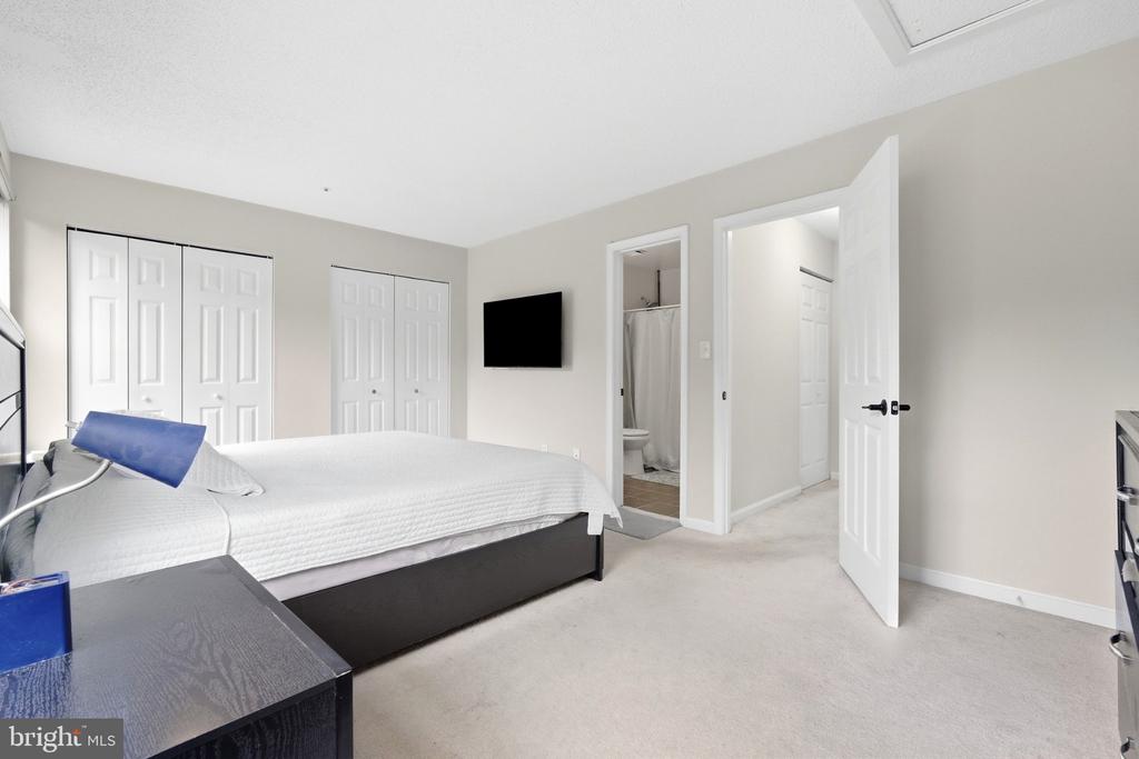 Bedroom with a white bed, dark dresser, closet doors, and an open bathroom doorway.