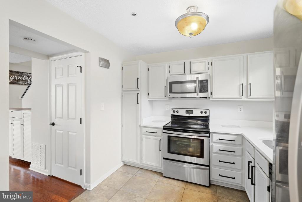 White kitchen with stainless steel range and microwave, shaker cabinets, and beige tile floor.