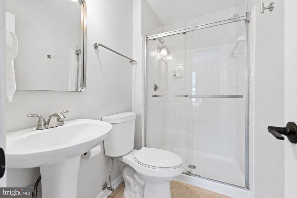 White bathroom with pedestal sink, toilet, and glass-enclosed shower.