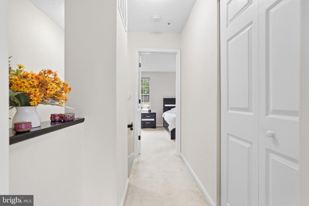 Carpeted hallway with paneled closet doors, a flower display, and a view into a furnished bedroom.