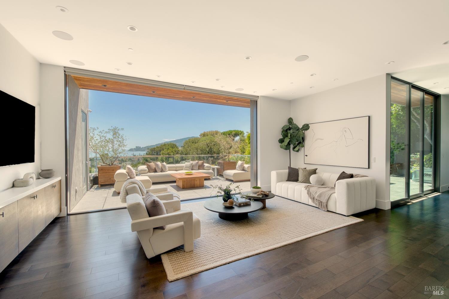 Modern living room opening onto a terrace with water and green hills beyond.