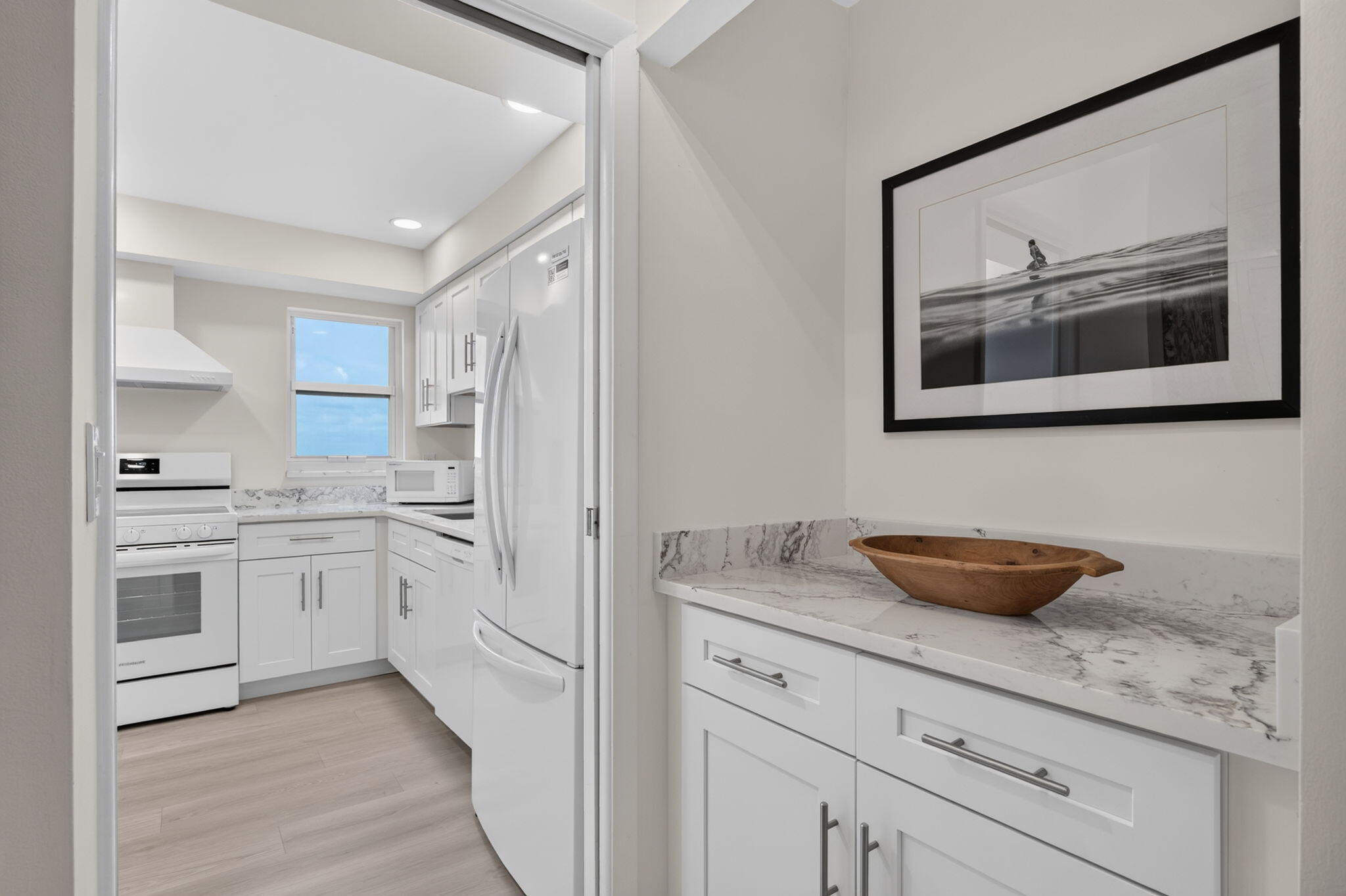 White kitchen with veined stone counters, white appliances, and a wooden bowl on the foreground counter.