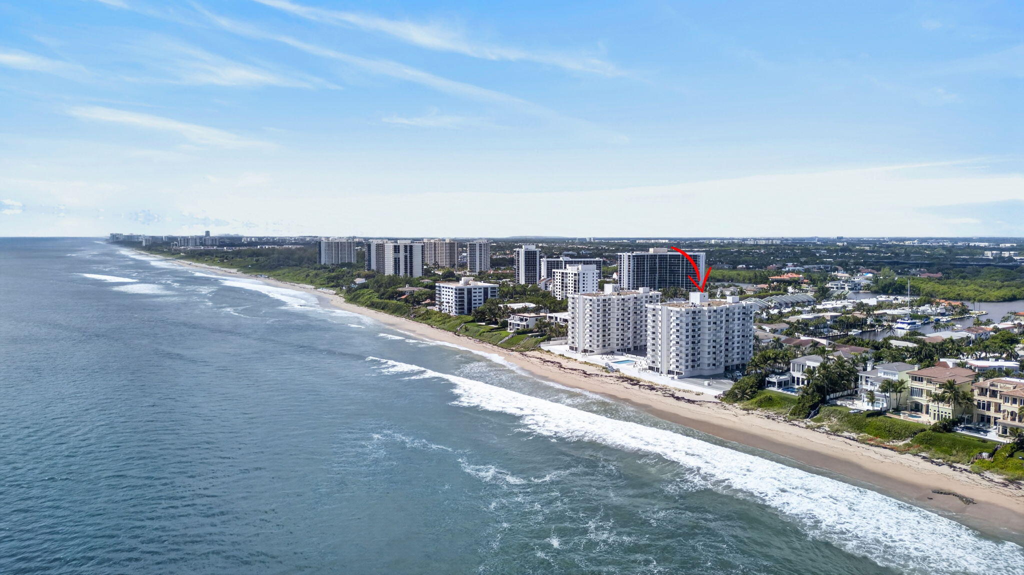 Aerial coastline with a red arrow marking an oceanfront condominium beside the beach.