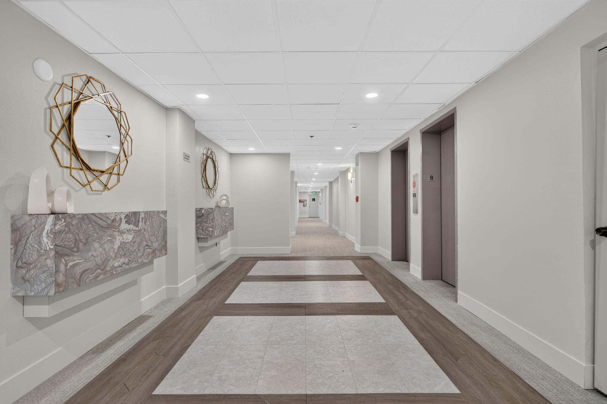 Condominium hallway with two elevators, geometric mirrors, and stone console tables.