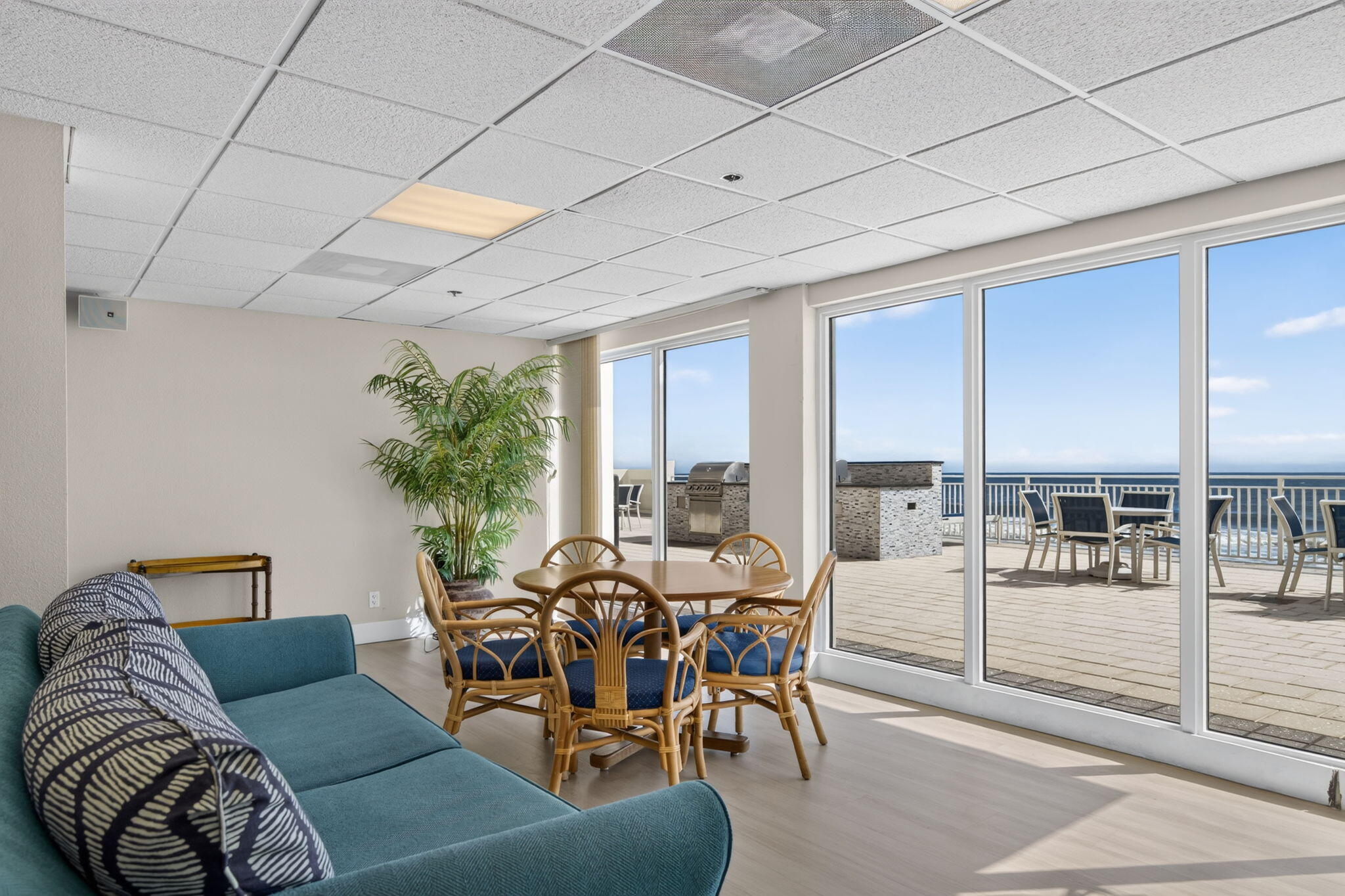 Condo living and dining area with teal sofa, rattan chairs, and balcony overlooking the ocean.
