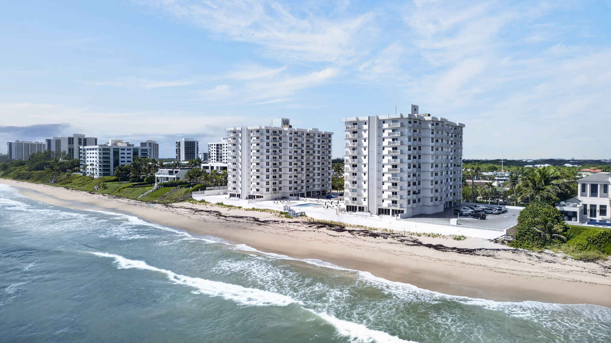 Beachfront condominium towers beside a sandy shore, with ocean waves and a pool.
