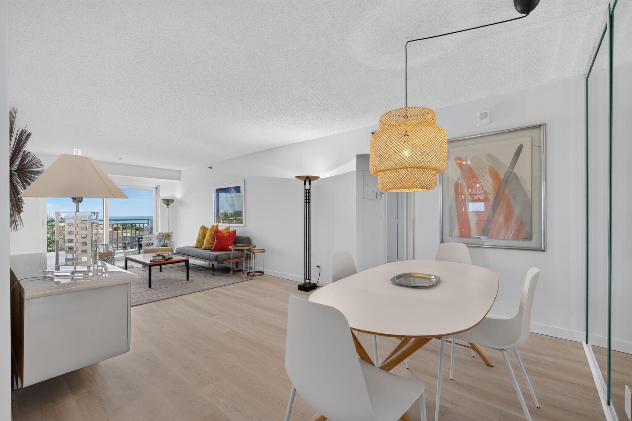 Open-plan living and dining area with a woven pendant light and ocean visible from the balcony.