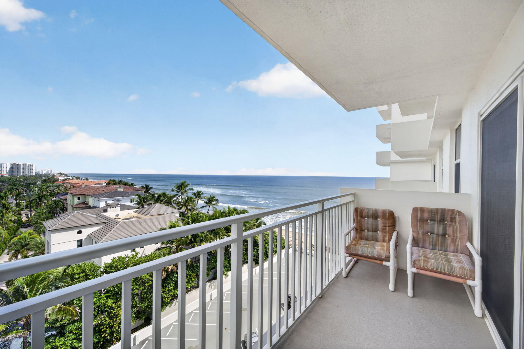 Oceanfront balcony with two cushioned chairs overlooking the Atlantic and palm-lined shoreline.