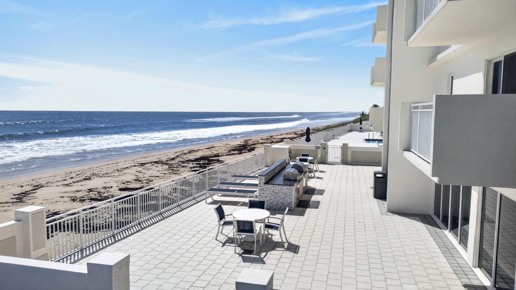 Oceanfront terrace with outdoor dining furniture, built-in grill, pool, and beach view.