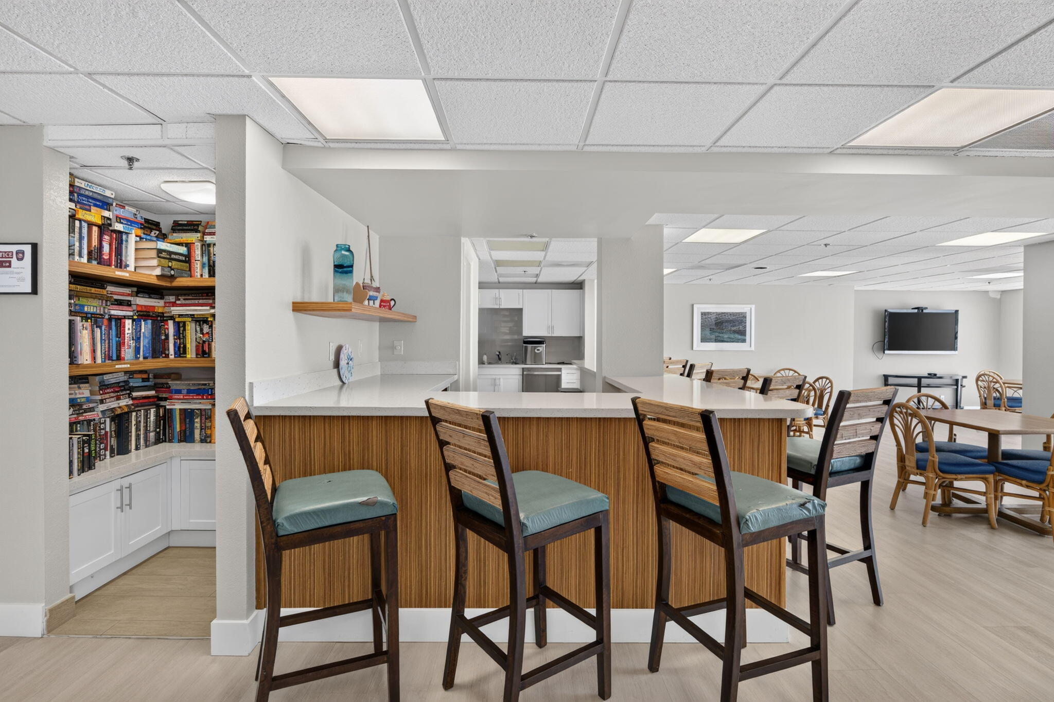 Communal lounge with a wood-fronted breakfast bar, book-filled shelves, and dining seating.