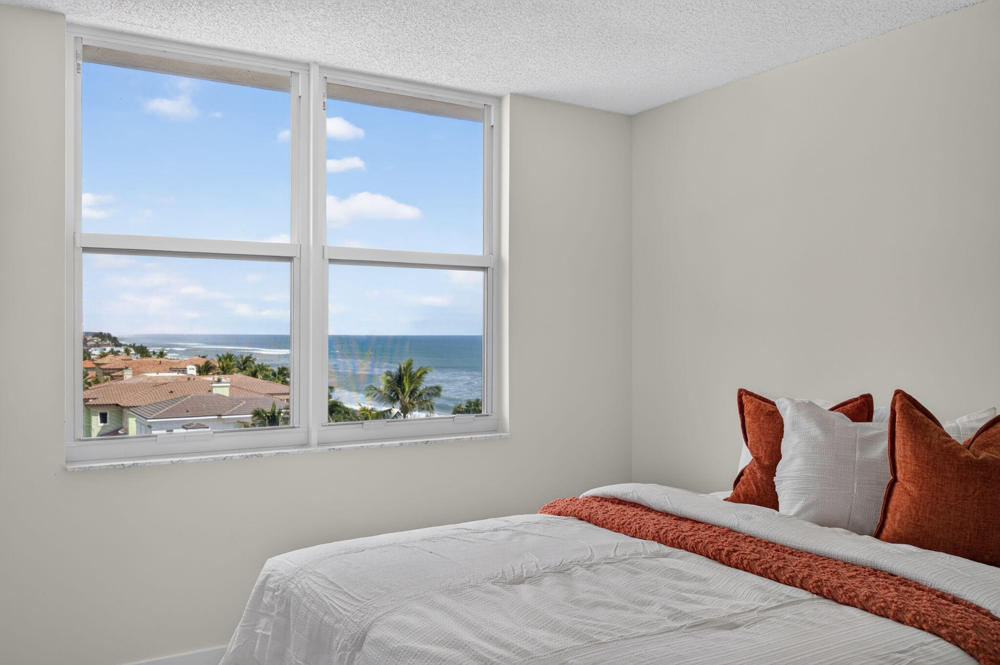 Bedroom with rust-colored pillows and large windows overlooking the ocean.