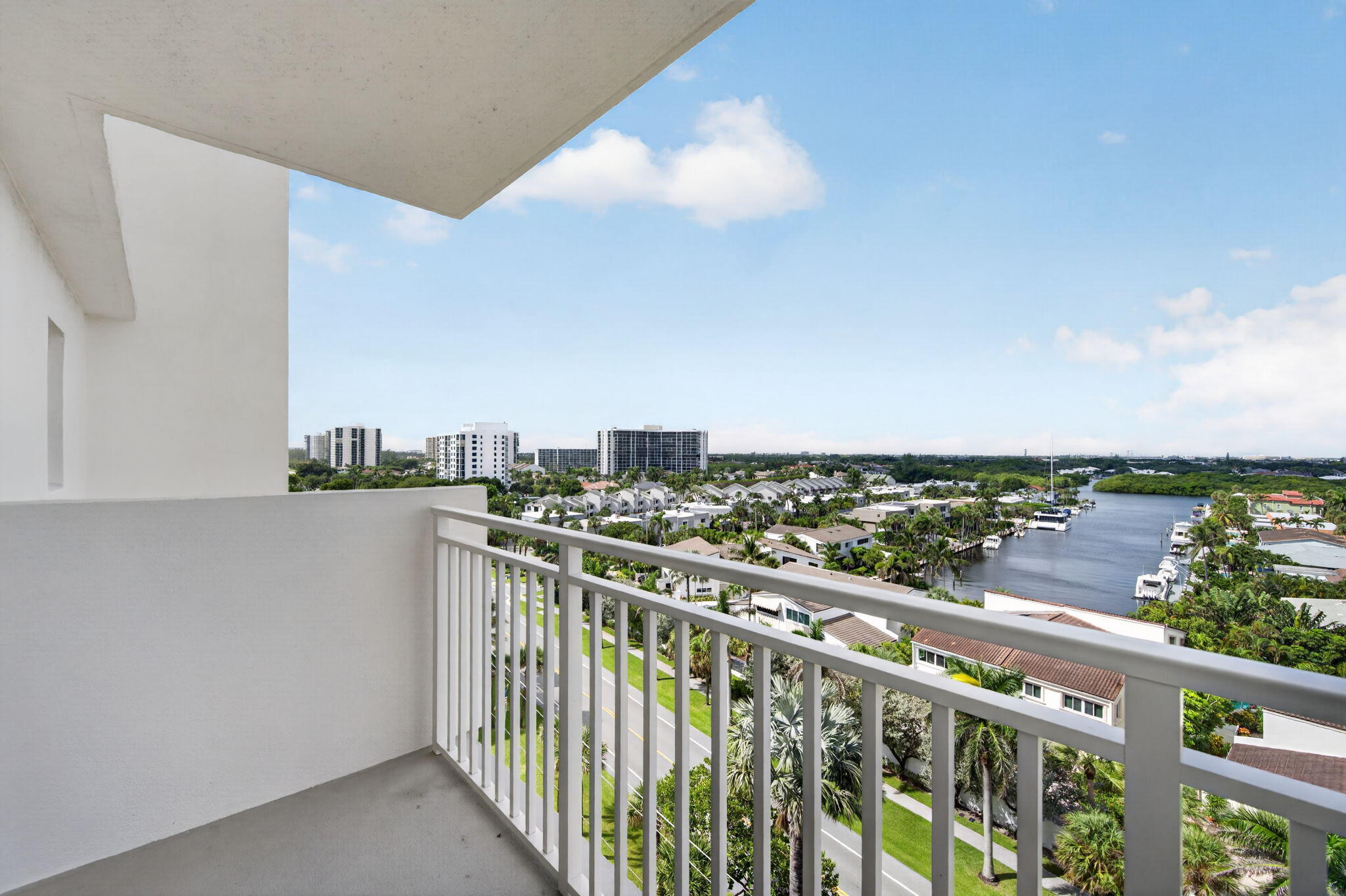 High-rise balcony overlooking a canal, boats, palm trees, and waterfront homes.
