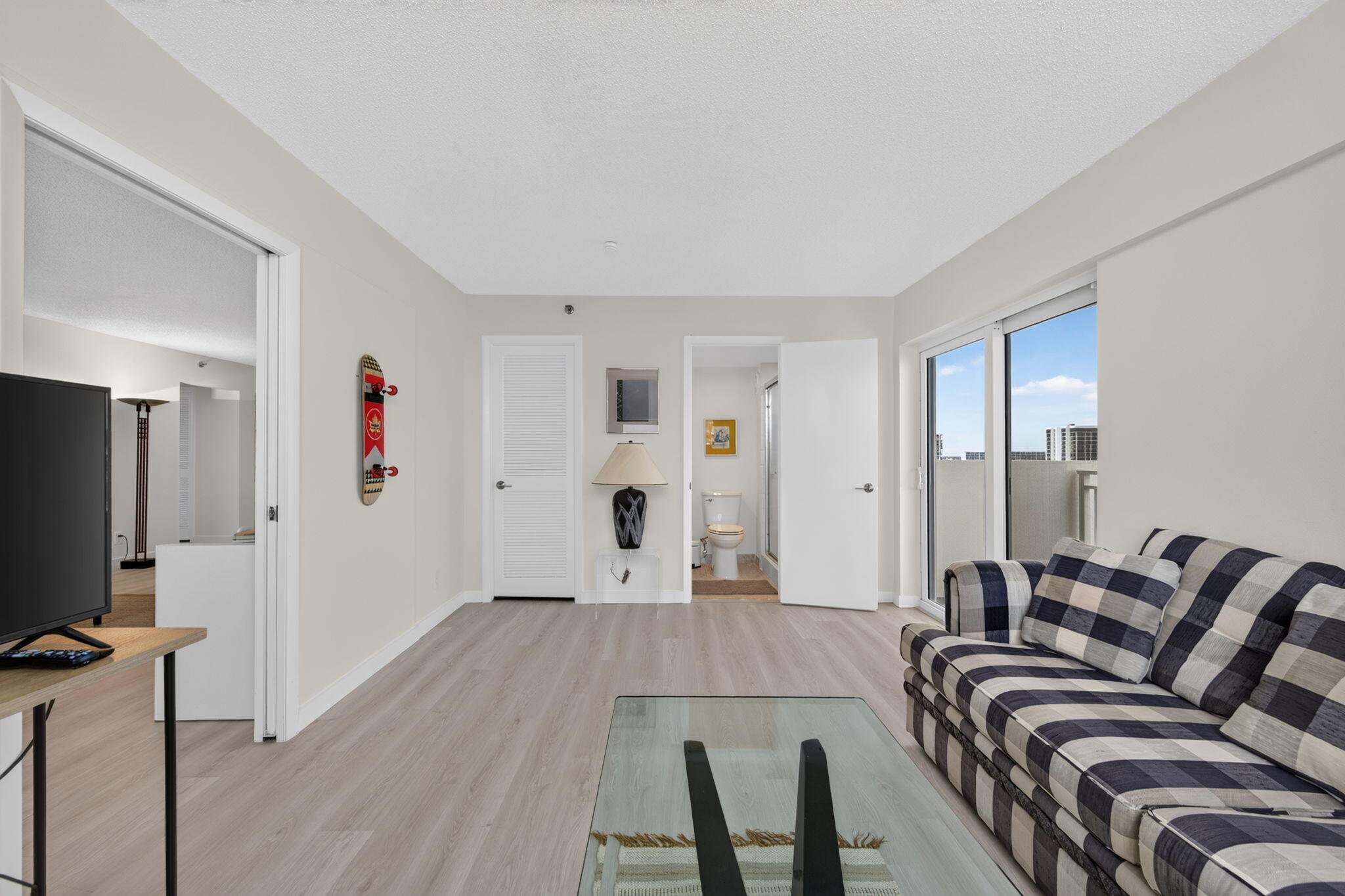 Living room with a plaid sofa, glass coffee table, and sliding doors to a balcony.