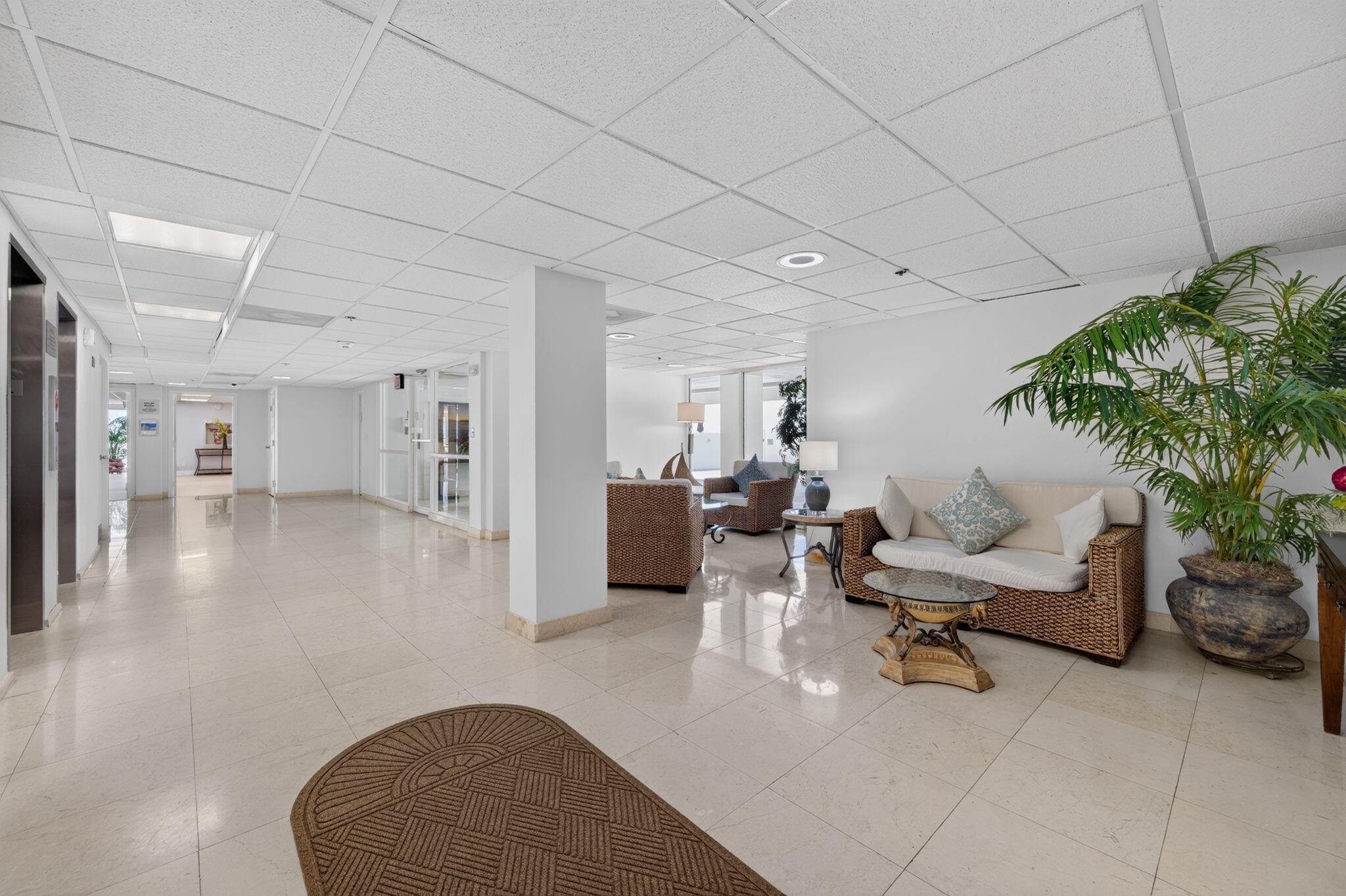Condominium lobby with a tiled hallway, wicker seating area, and large potted palm.