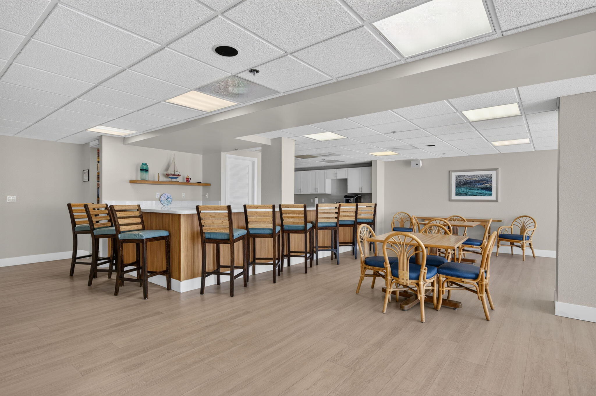 Furnished communal dining room with a long counter, bar stools, wicker tables, and a kitchenette.