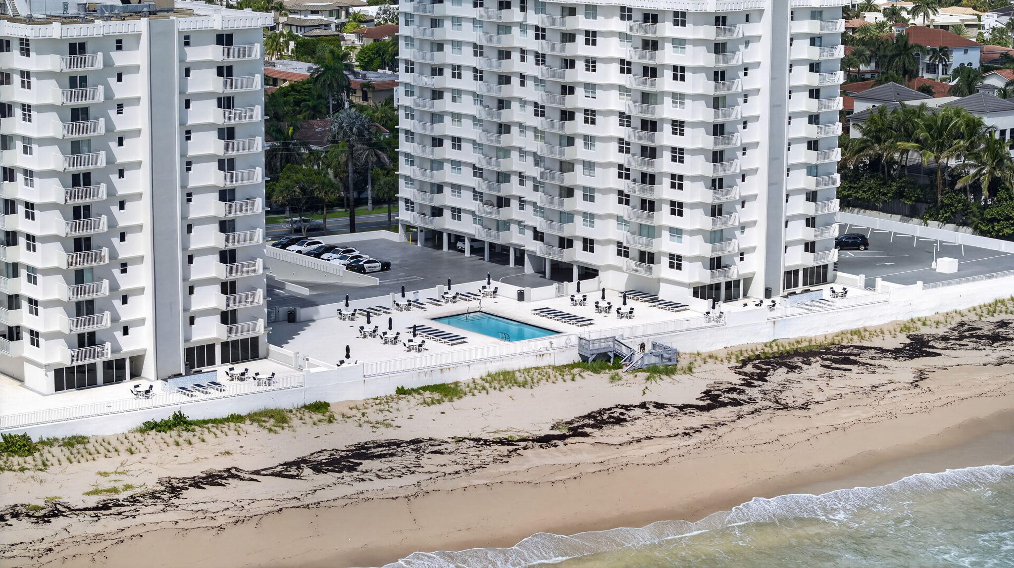 Beachfront condominium towers with a pool and lounge deck overlooking the sandy shore and ocean.