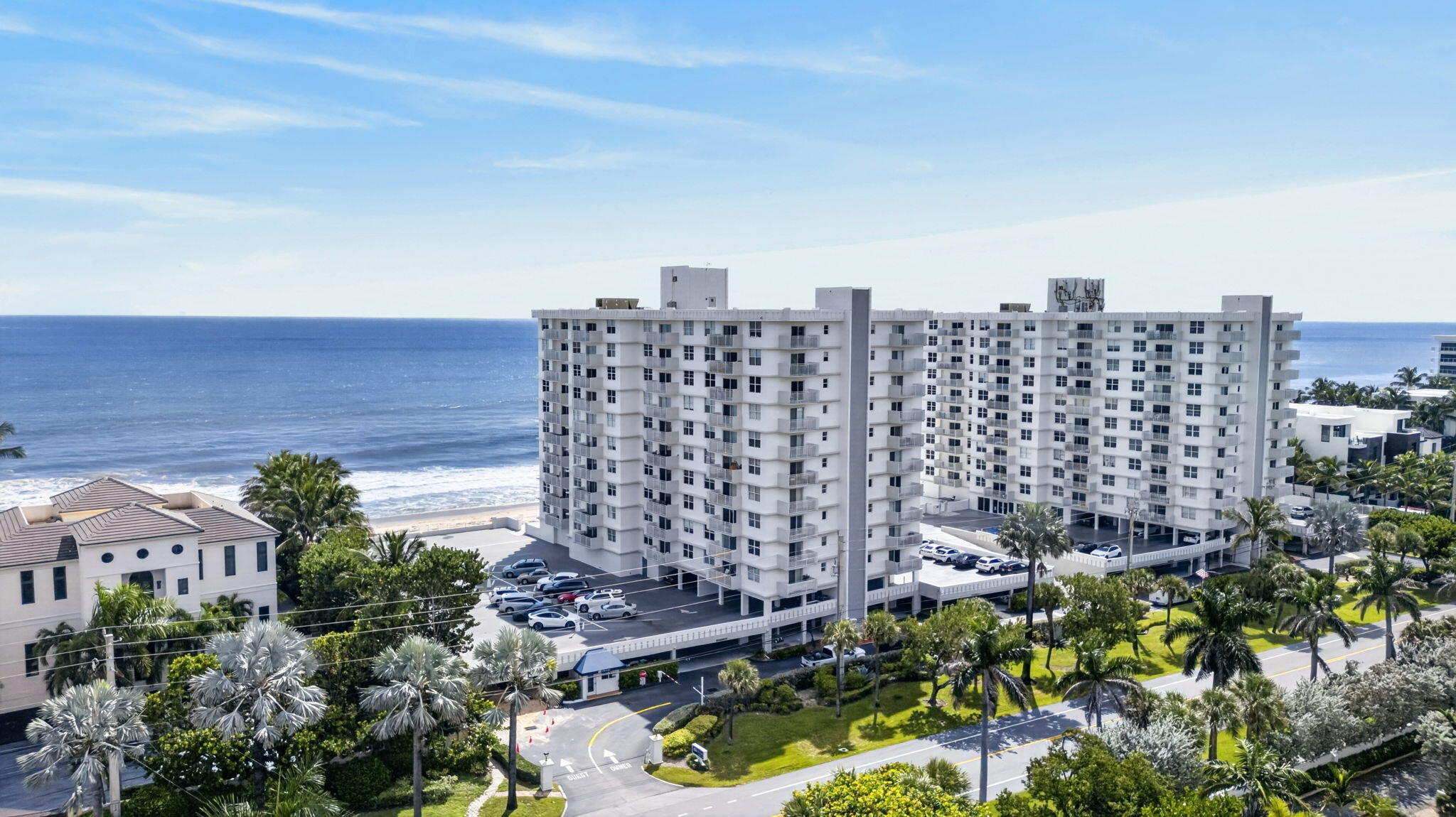 Beachfront condominium building beside the ocean, surrounded by palm trees.