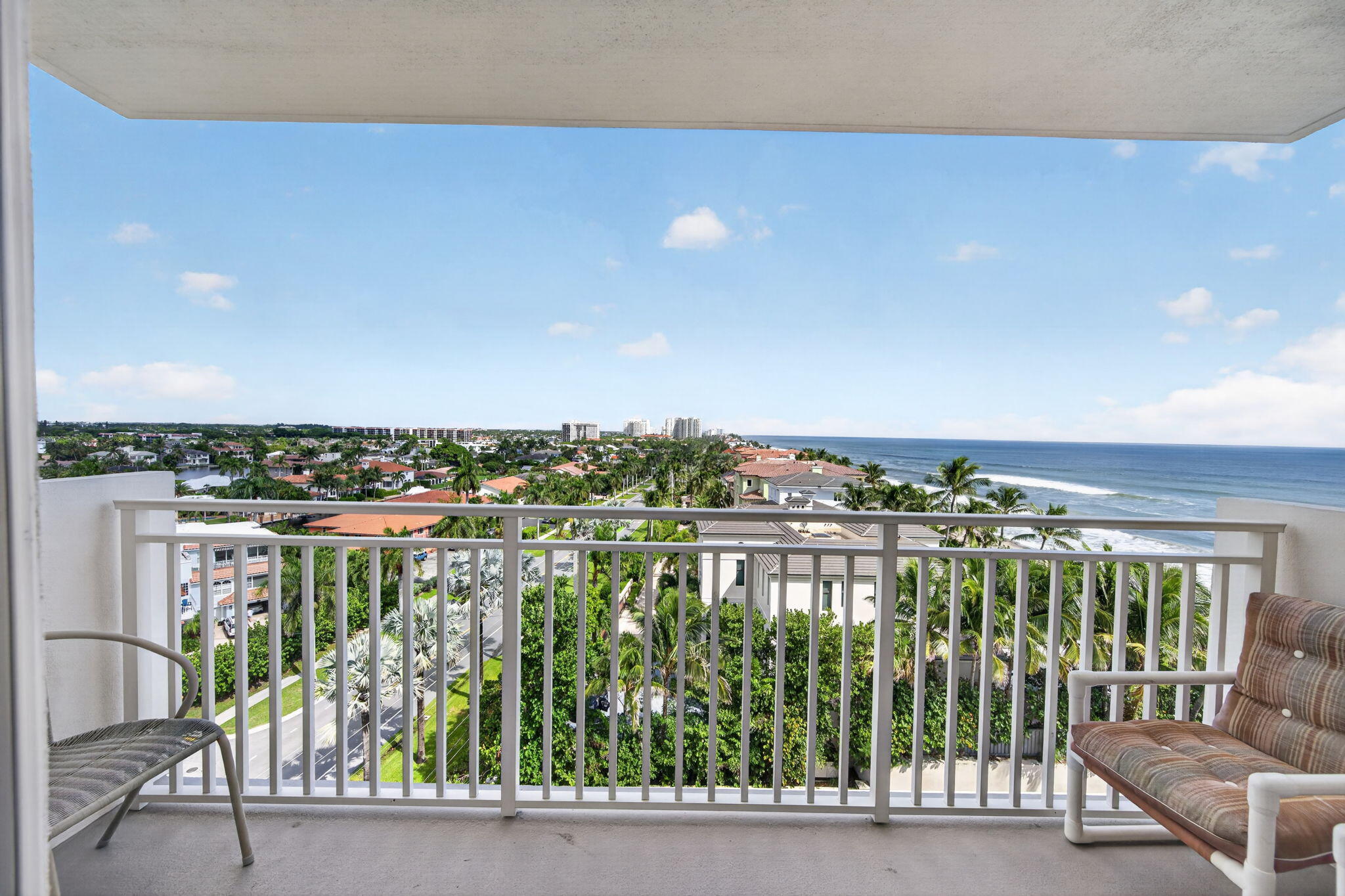 Balcony overlooking the Atlantic Ocean and palm-lined coastal homes, furnished with two chairs.