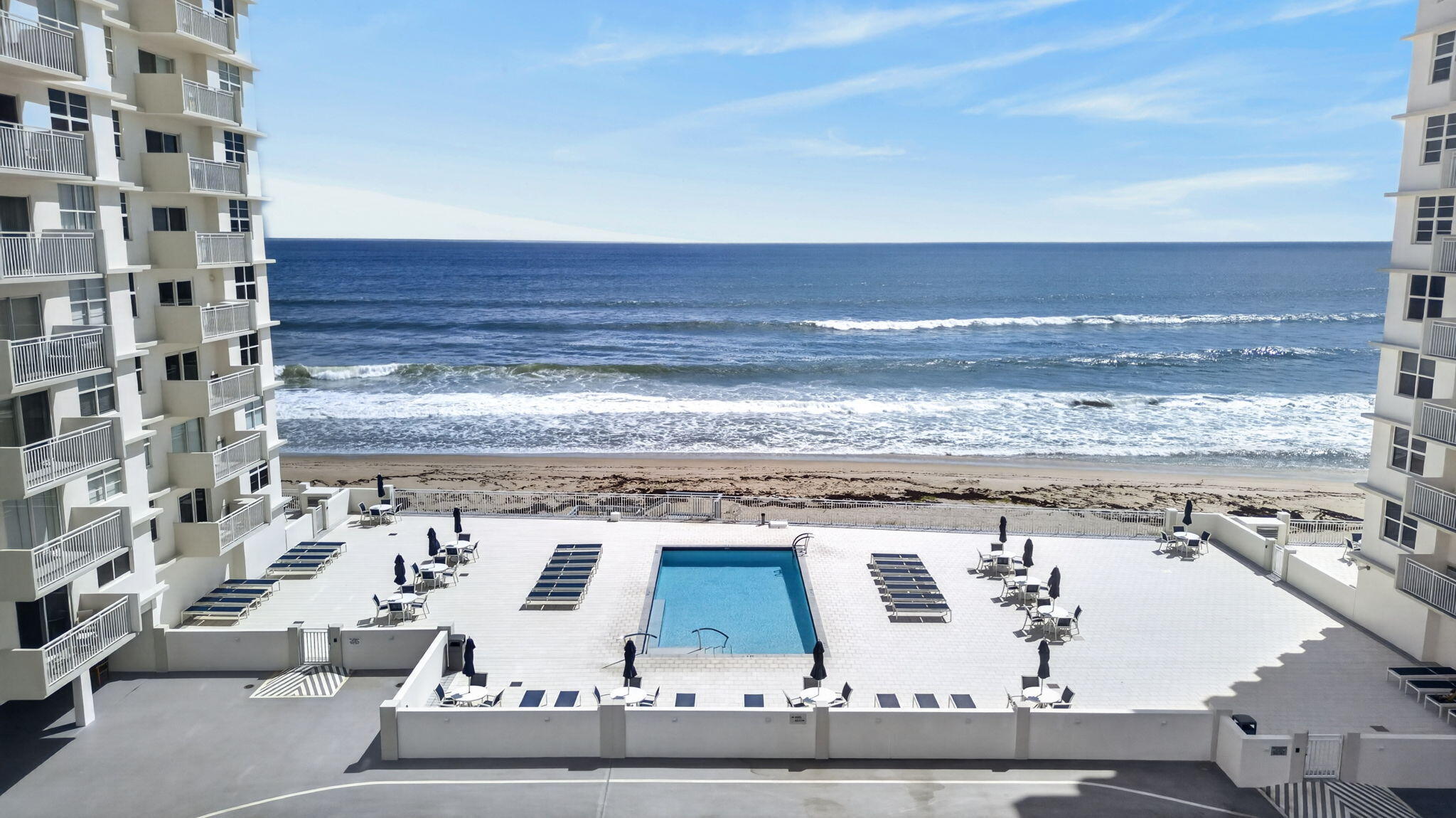 Oceanfront condominium pool deck with lounge chairs, framed by the beach and ocean.