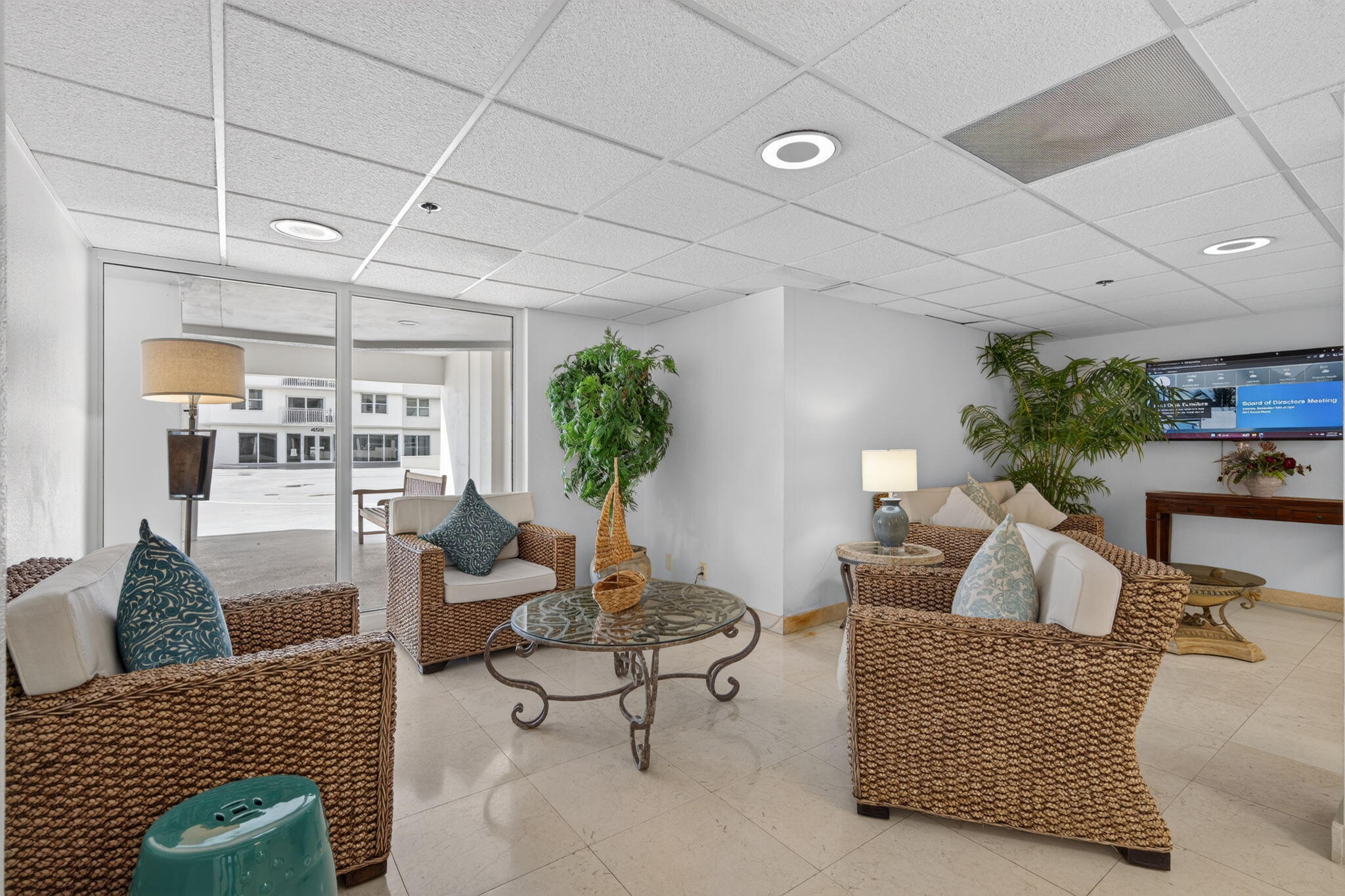 Condominium lobby lounge with wicker seating, a glass coffee table, and potted palms.