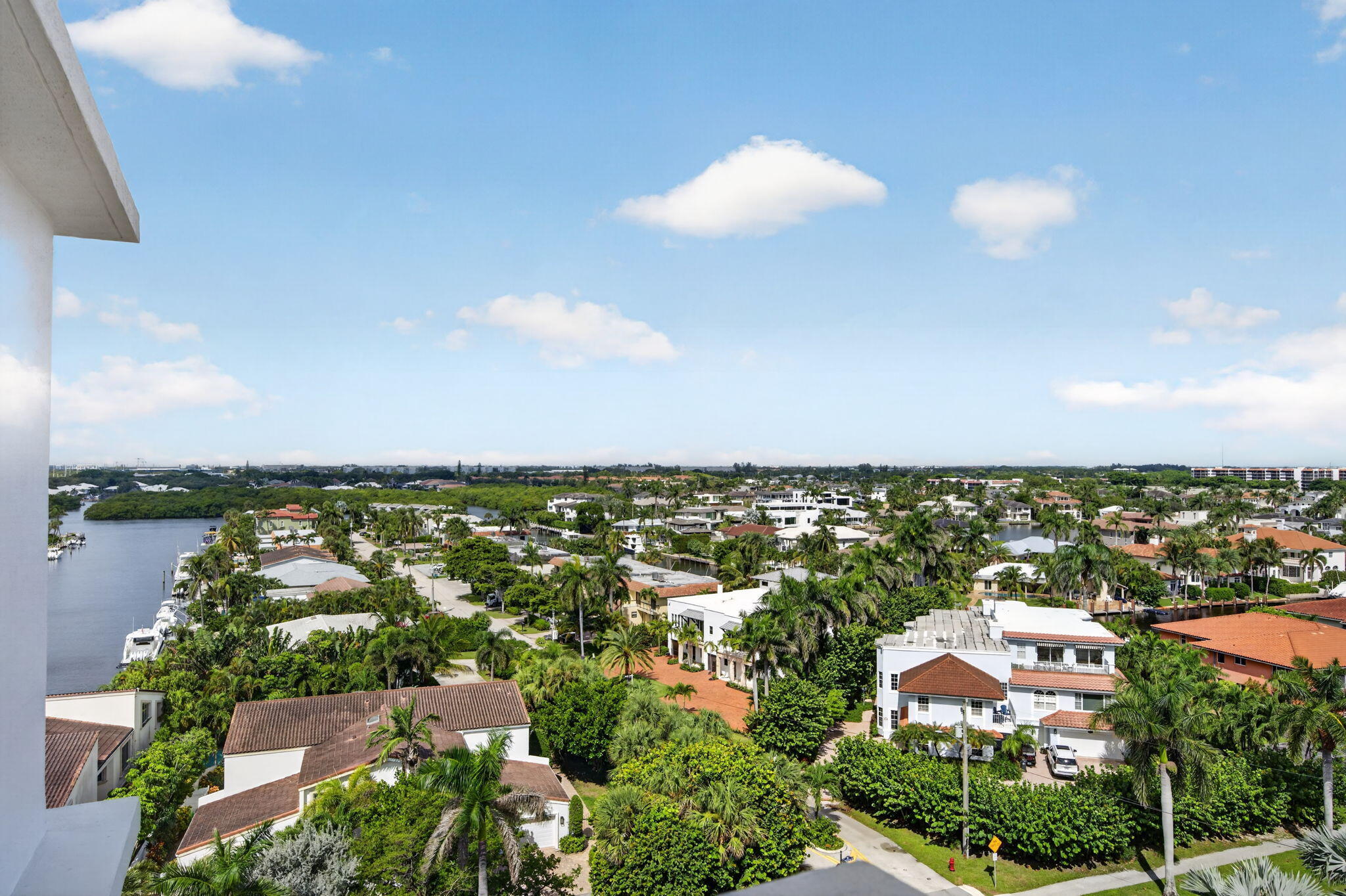 Panoramic view of palm-lined homes and a waterway from a high-rise balcony.