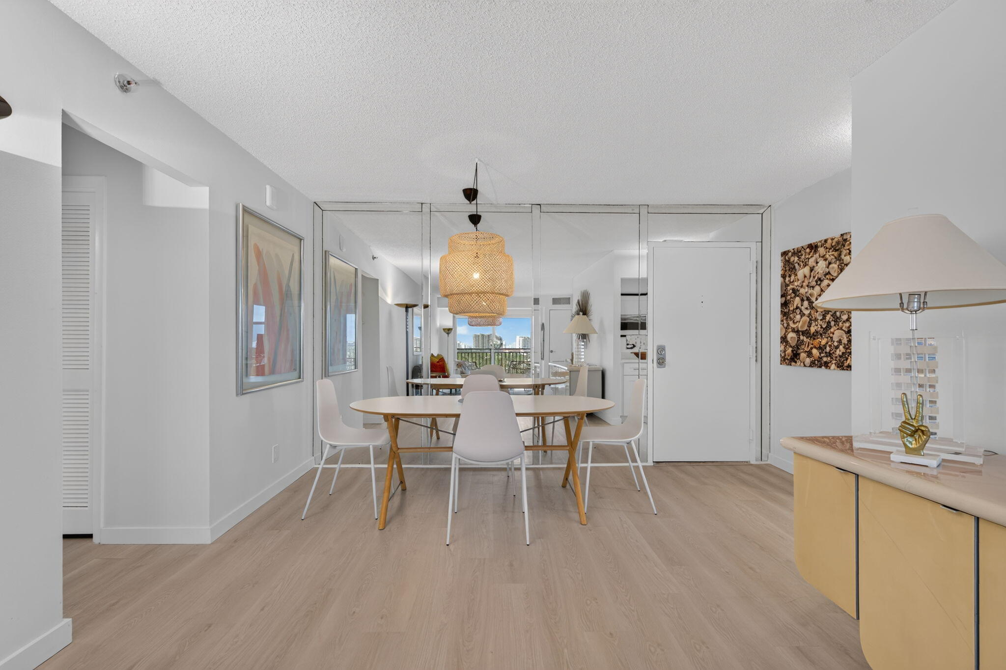 Furnished dining area with a woven pendant light, mirrored wall, and city view through balcony doors.