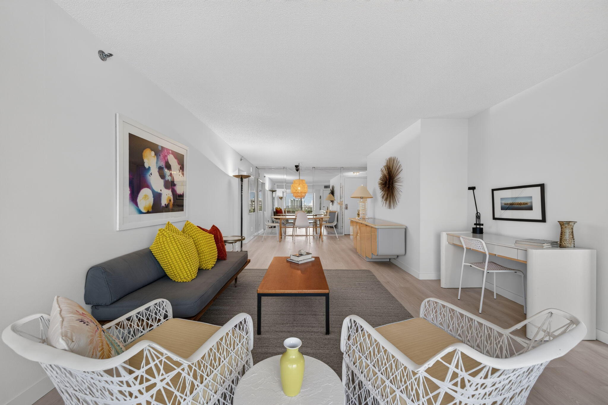 Open-plan living room with a gray sofa, yellow cushions, white chairs, and a dining area beyond.
