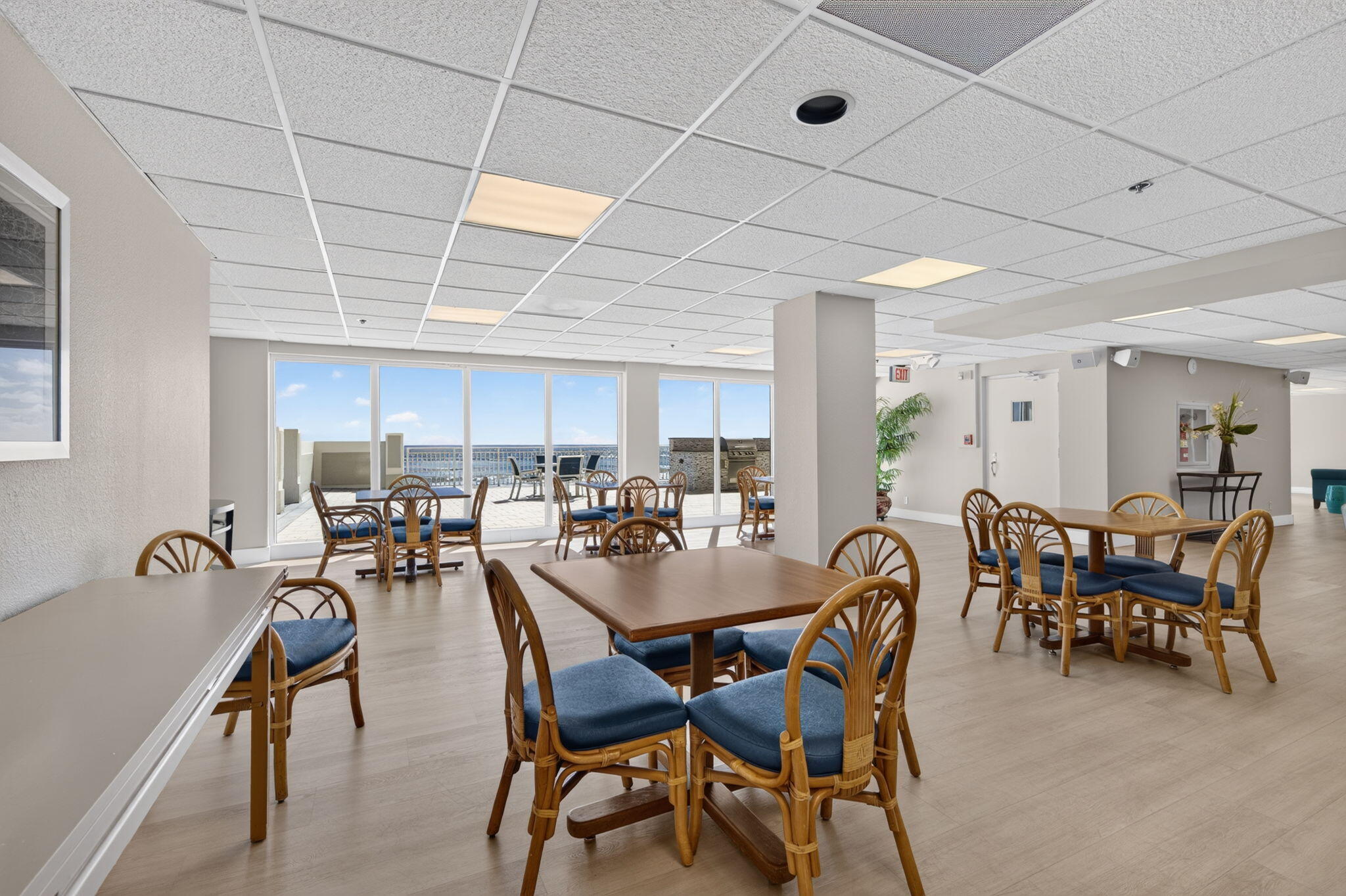 Communal dining room with wicker chairs and tables beside windows overlooking the ocean.