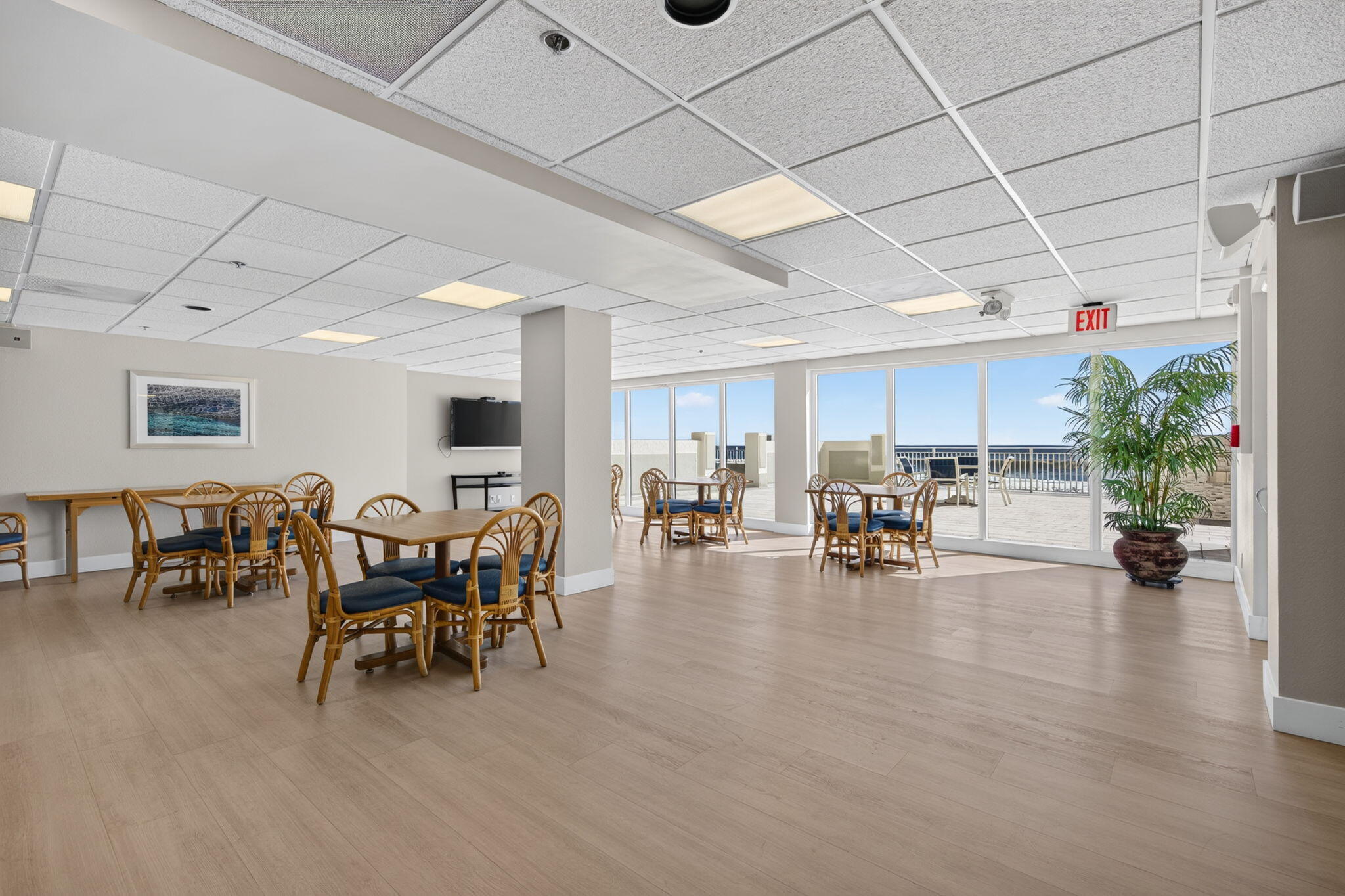 Furnished communal lounge with wicker seating, glass doors, and a terrace overlooking the water.