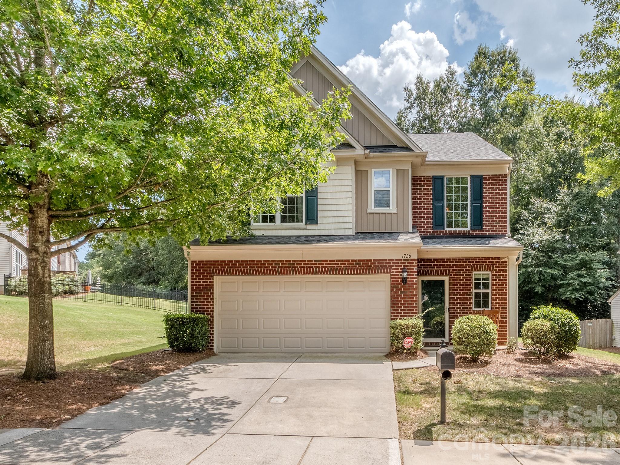 Two-story brick-and-siding house with an attached double garage, driveway, and large shade tree.