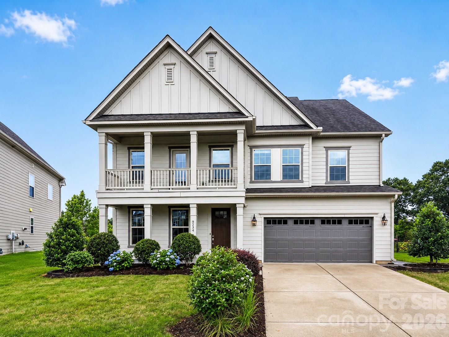 Two-story white house with a front balcony, landscaped shrubs, and a double garage.