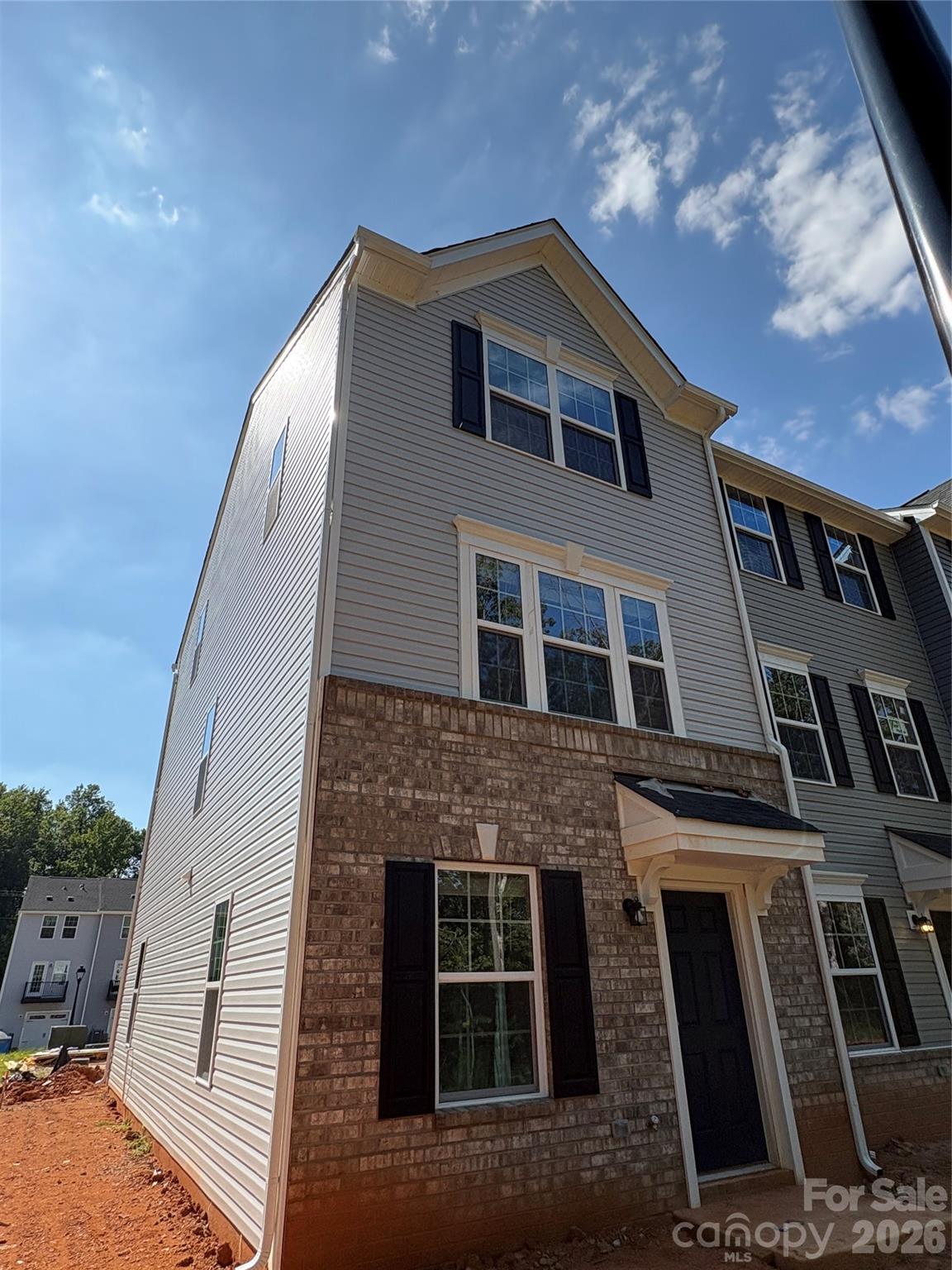 Attached townhouse with gray siding, brick facade, black shutters, and a covered front entry.