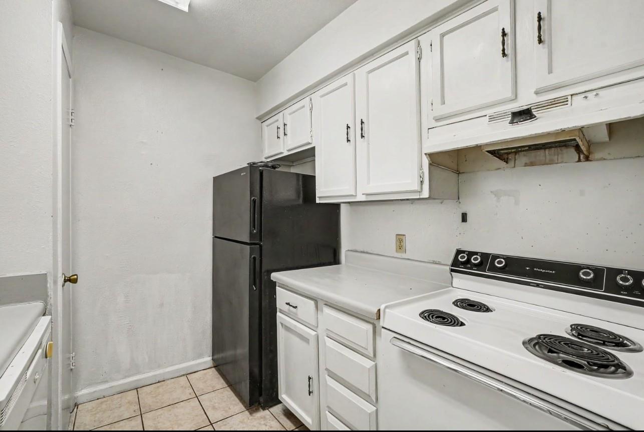 Kitchen with white cabinets, black refrigerator, and white electric coil range.