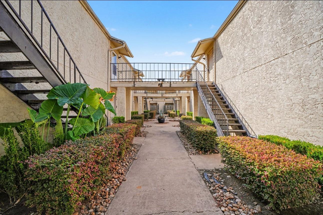 Apartment courtyard with a paved walkway, connecting bridge, metal stairs, and landscaped beds.