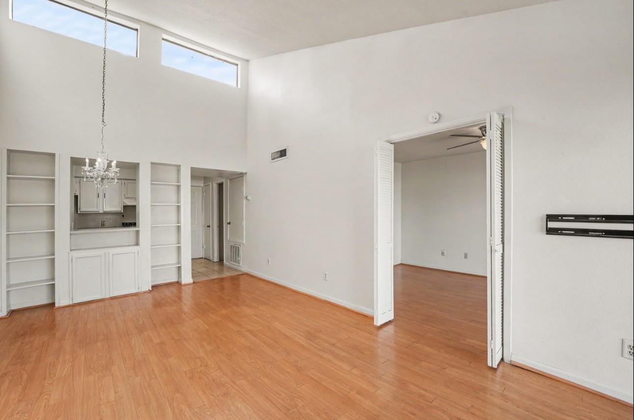 Unfurnished living room with wood floors, built-in shelves, and high windows.