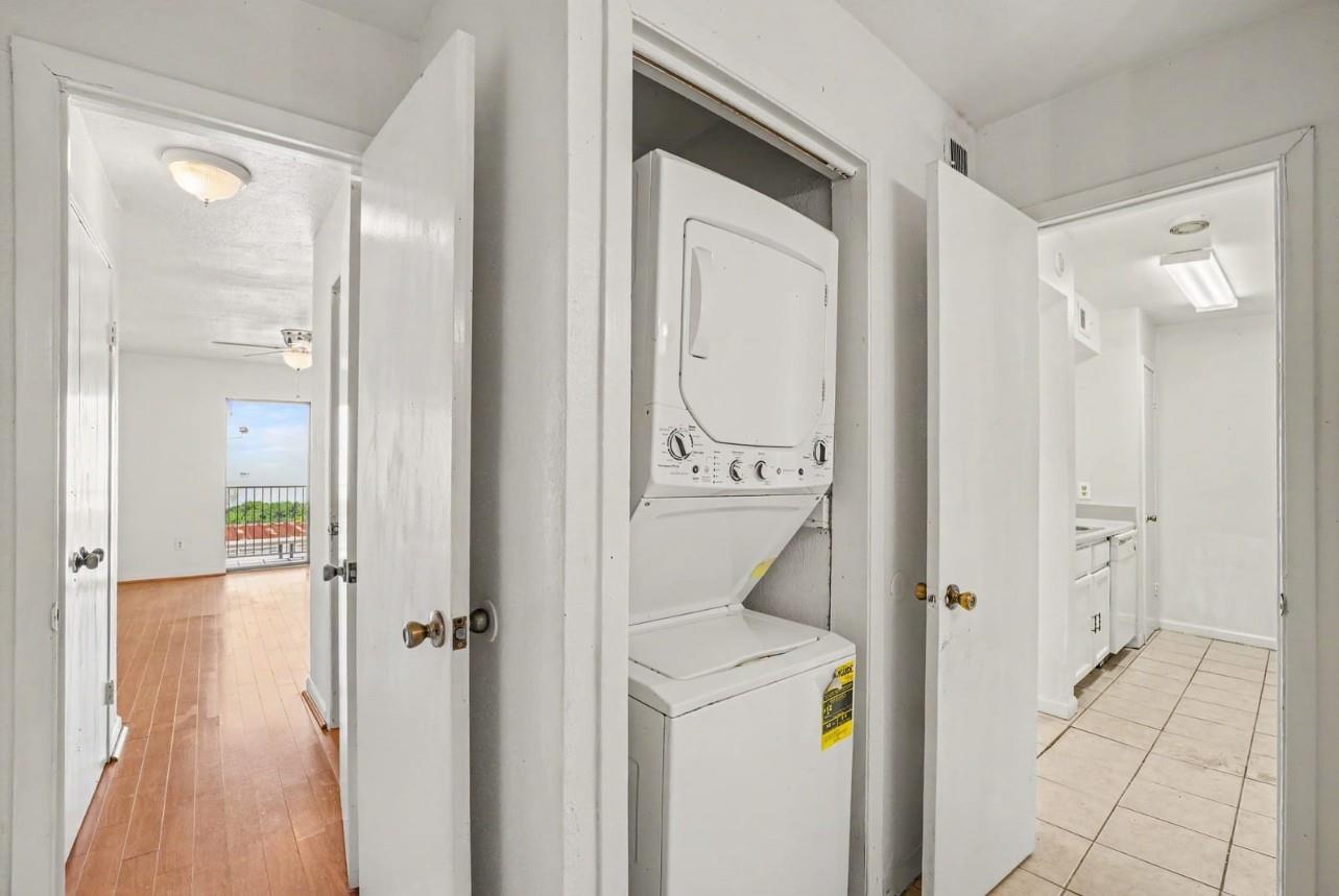 Laundry area with a stacked washer and dryer, bathroom doorway, and wood-floored room beyond.
