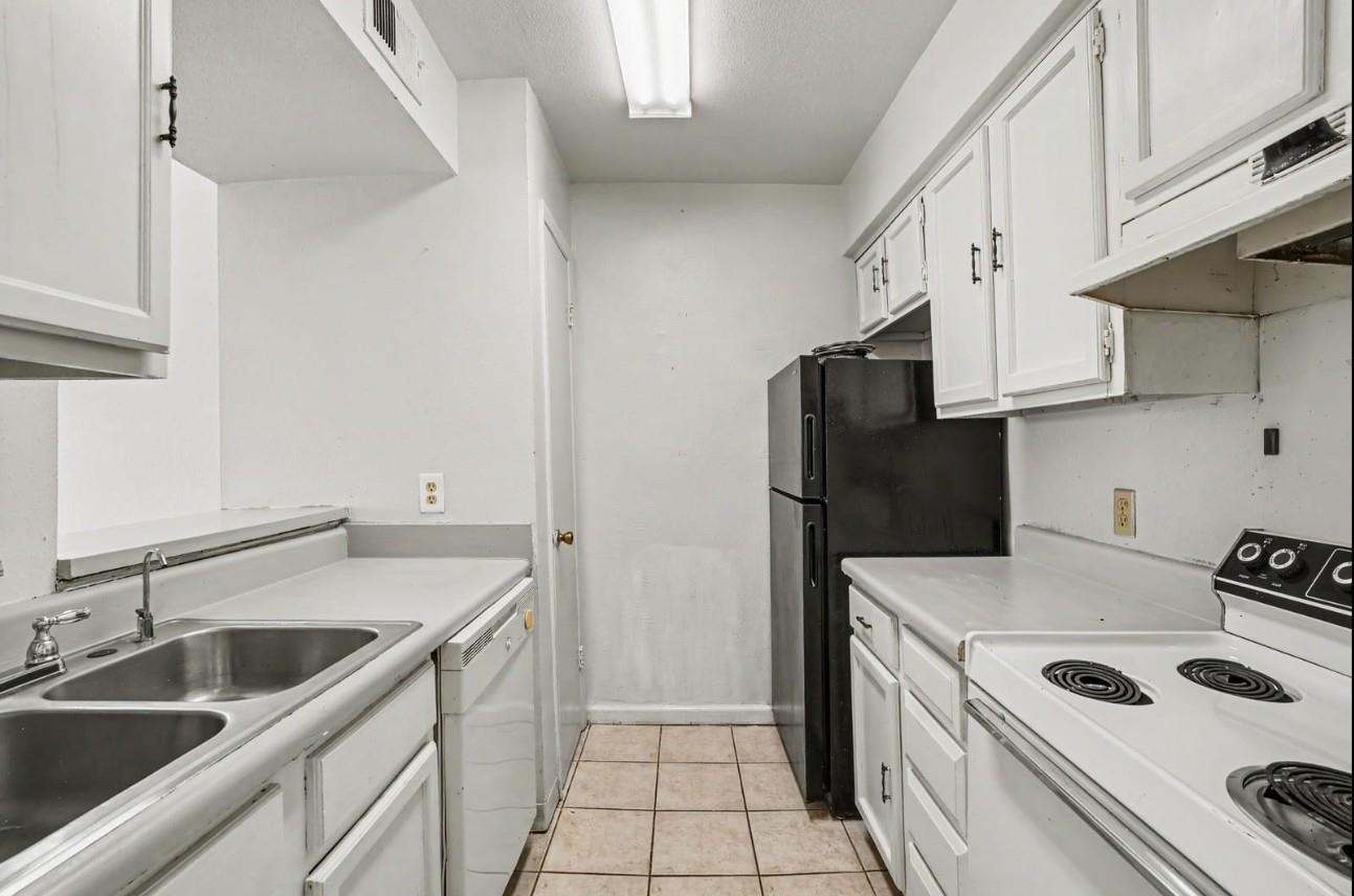 Narrow kitchen with white cabinetry, a double sink, electric range, and black refrigerator.