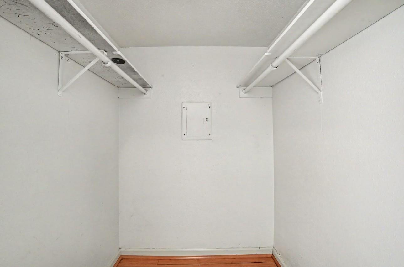 Empty walk-in closet with overhead shelves, side-by-side hanging rods, and a wood floor.