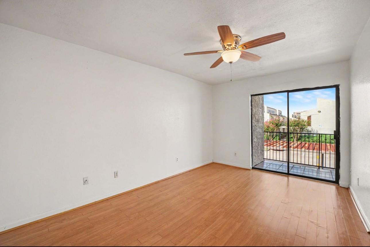 Empty living room with wood-look floors, a ceiling fan, and sliding glass doors to a balcony.