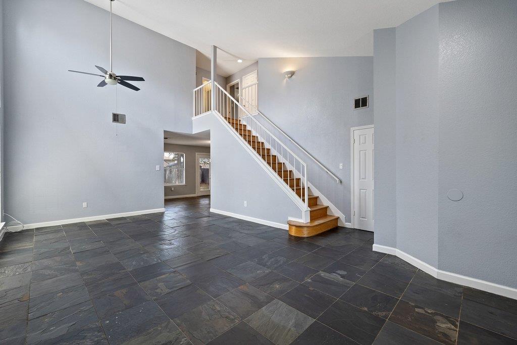 Vacant two-story living area with dark slate tile flooring and a white-railed staircase.