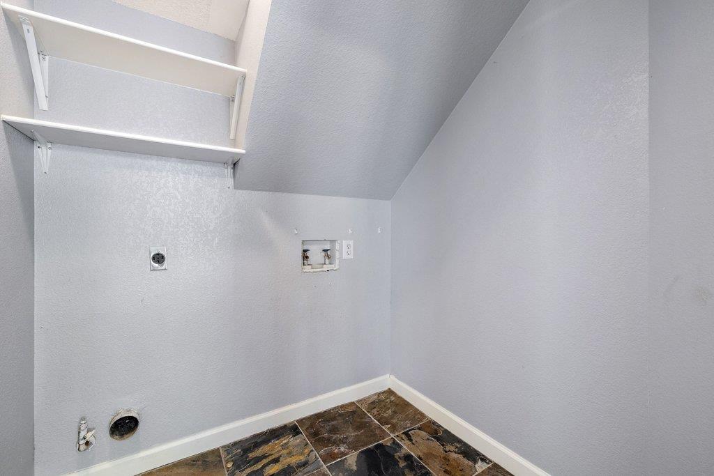 Empty laundry room with wall shelves, washer and dryer hookups, and dark patterned tile flooring.
