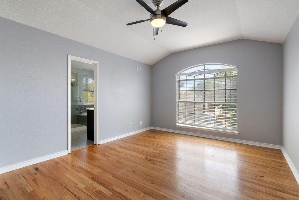 Empty bedroom with wood floors, vaulted ceiling, ceiling fan, and arched window.