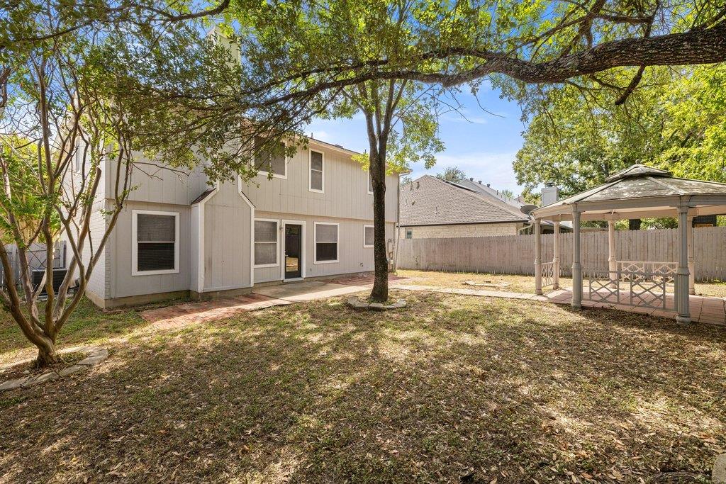Two-story home’s backyard with mature trees and a covered gazebo.